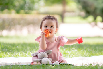 adorable and happy baby girl playing outdoors in the park - portrait of 7 or 8 months old beautiful little child smiling cheerful sitting on mat on grass at city park playing with plastic blocks