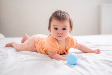 Fototapeta premium lifestyle home portrait of happy and beautiful 8 months old baby girl mixed race Asian Caucasian playing with ball cheerful on bed and exploring the surroundings curious