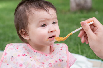 woman feeding her beautiful little daughter - mother hand and close up portrait of adorable and happy baby girl eating baby porridge from spoon in health and nutrition concept