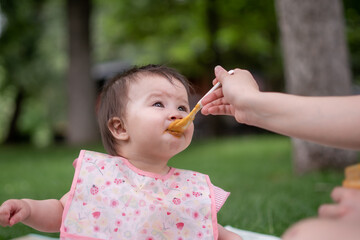 woman feeding her beautiful little daughter - mother hand and close up portrait of adorable and happy baby girl eating baby porridge from spoon in health and nutrition concept