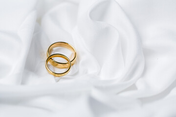 Golden wedding rings for engagement. Marriage golden rings with white, pink ribbons background. Rings on the white and red rose. The marriage rings is the symbol of traditional wedding of pair lovers.