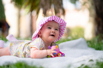 adorable and happy baby girl hat embraces the joys of playfulness on a soft blanket playing with little toy. Laughing as she explores the natural wonders of an outdoors city park