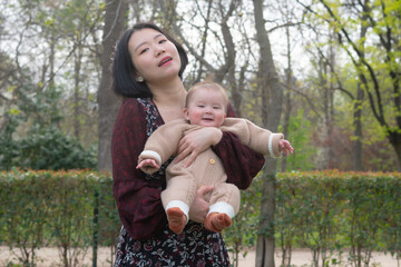 Fototapeta premium young happy and beautiful Asian Chinese woman holding little daughter, a cute an adorable baby girl, playful together in the park in mother and child love and parenting concept