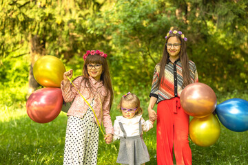 Fototapeta na wymiar Three girls, sisters holding hands on a field with balloons in hand, colorfully dressed