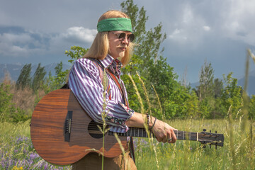 Hippie guy with a guitar in a forest clearing on a sunny day