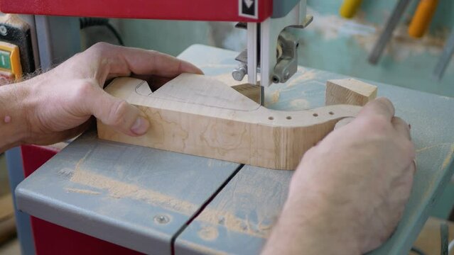 A violin maker cuts a blank for making a violin scroll on a bandsaw, close-up.