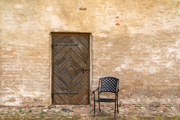 Fototapeta na wymiar An empty metal chair against old house with a wooden door