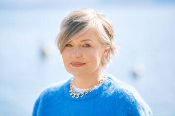 Outdoor portrait of beautiful 55 - 60 year old woman, wearing blue pullover