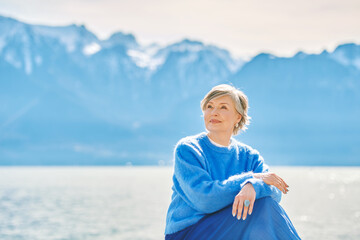 Outdoor portrait of beautiful mature woman relaxing next to lake, wearing warn cozy pullover,...