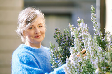 Outdoor portrait of mature woman smelling rosemary herb - 614413447