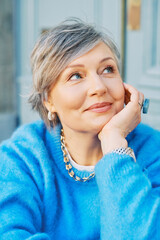 Outdoor portrait of beautiful 55 - 60 year old woman, wearing blue pullover