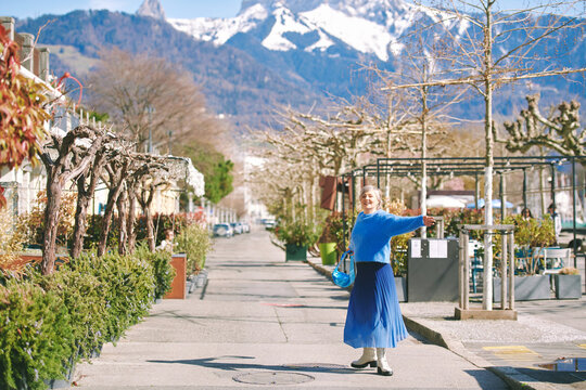 Outdoor Portrait Of Mature 55 - 60 Year Old Woman Walking Down The Street, Wearing Blue Skirt And Pullover. Image Taken In Vevey, Switzerland