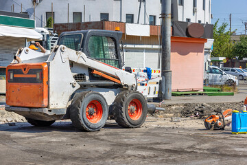 A highly manoeuvrable construction vehicle with a jackhammer attached is parked at a work site with...