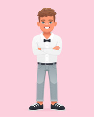 A happy little boy stands with his arms crossed. A beautiful cute schoolboy child in a white shirt with a bow tie.