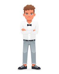 A disgruntled little boy stands with his arms crossed. A beautiful cute schoolboy child in a white shirt with a bow tie.