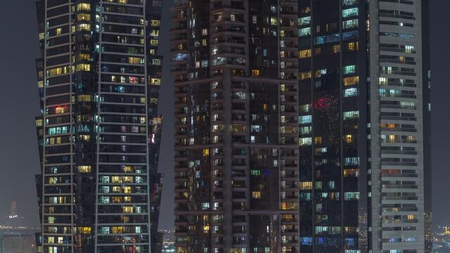 Tall blocks of flats with glowing windows located in residential district of city aerial timelapse. Evening light in rooms in high-rise towers and skyscrapers