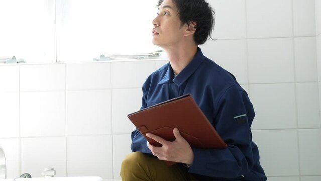 風呂場をチェックする作業着を着た日本人男性	