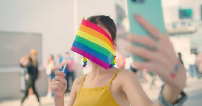 Young beautiful woman holding rainbow flag at city street. She talking to phones with attractive smiling.