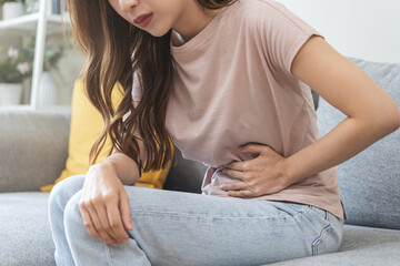 Flatulence asian young woman intolerance hand in stomach ache, suffer from food poisoning, abdominal pain and colon problem, gastritis or diarrhoea when at home. Patient belly, abdomen or inflammation