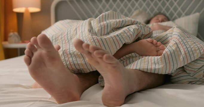 moving female and male's feet under stiped blanket, closeup cropped view slow motion