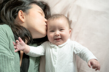 love and playfulness, a young Asian Chinese woman joyfully engages with her baby girl on the bed. Their laughter creates precious memories together bonding in pure happiness