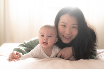 love and playfulness, a young Asian Korean woman joyfully engages with her baby girl on the bed. Their laughter creates precious memories together bonding in pure happiness