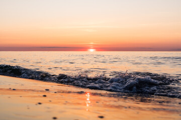 Orange sunset at a beach of the baltic sea on the German island Rugia with breaking wave in the foreground