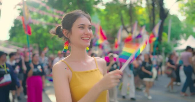 Young beautiful woman holding rainbow flag at city street. She enjoying with LGBT parede in event.