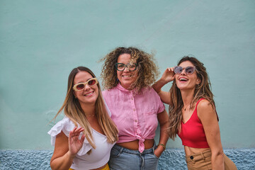 three girl friends in their 30s posing amusingly in front of an aquamarine wall