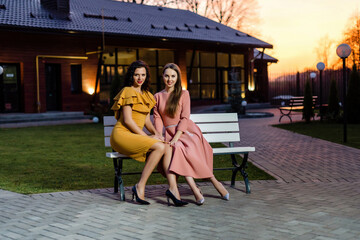 Beautiful young women in dresses are sitting on a wooden bench. Country house near the forest.