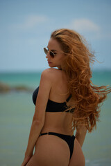 Beautiful young woman in black bikini and sunglasses on the beach.