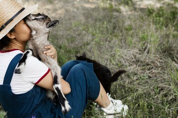 Farmer asian woman holding baby goat in her arms on a farm.