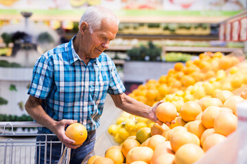 Elderly retired man buying oranges and grapefruits in grocery department of supermarket