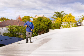 A man doing high pressure spray cleaning of a roof in preparation of painting, in Worcester,...