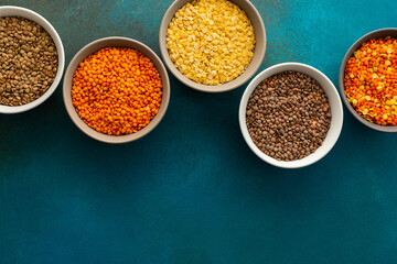Multicolored lentils in bowls on an emerald green background, yellow and brown, green and orange lentils, healthy legumes, top view, copy space