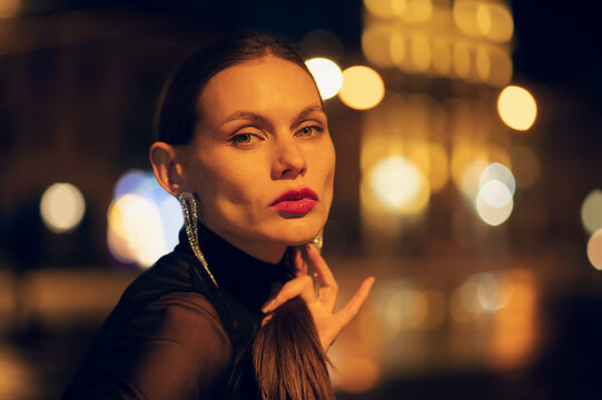 Beautiful fashionable confident woman wearing trendy rhinestone earrings, black mesh top,  posing among night lights in street of city. Outdoor close up portrait. Copy, empty space for text - Powered by Adobe