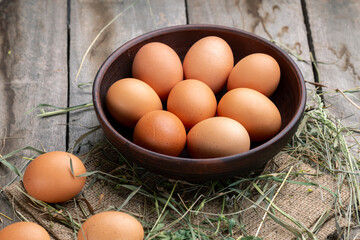 Brown chicken eggs in a bowl on a background of hay and wooden boards.