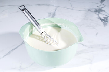 Liquid dough in an iron bowl with a whisk. Preparing dough for a sweet pie , stir the dough with a...