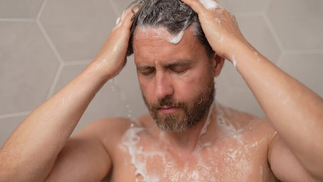 Hispanic man washing hair in bathroom. Guy bathing shower head in bathtub. Male face in shower. Man taking shower in bathroom. Guy showering. Bathroom concept. Man is under water drops in bathroom.