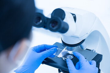 Women scientist looking to microscope eyepiece in clinical laboratory.Young scientist doing some research.Medical technician analysis blood slide on exam plate microscopic at laboratory department.