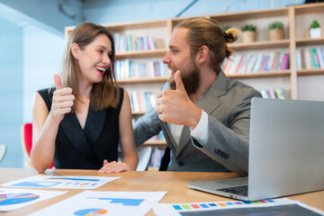Male and female colleagues sitting and discussing work together on laptops in conference room.