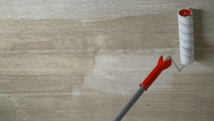 A worker applies paint to the ceiling with a hand roller at home. Priming the ceiling with a roller put on a long stick, close-up. Priming ceiling roller.