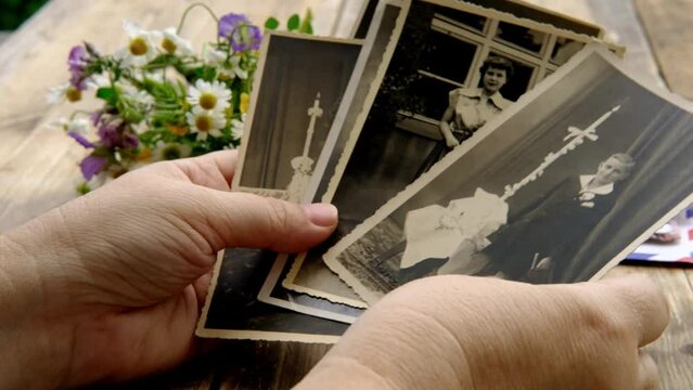 female hands holding paper envelope with old photographs, bouquet of wild flowers on table wooden table in garden, blurred natural background, concept of genealogy, memory of ancestors, family tree