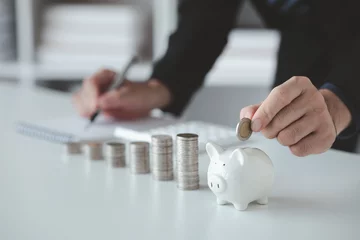 Fotobehang Person with pile of coins and piggy bank, money saving concept for future use and financial stability, salary management, personal finance, investment savings. © PhotosD
