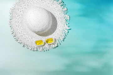 Top view summer white sun hat and colored sunglasses at sunlight glare, on blurred teal trend color background, sunlight glare as sea wave, copy space. Life style summer vacation photo minimal