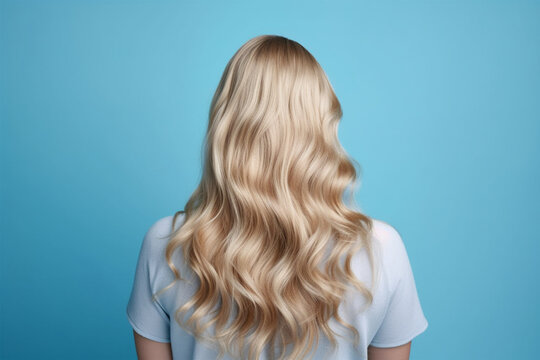 Beautiful young woman with blond stylish wavy hairdo on blue background, back view