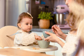 Young mom feeding her baby daughter with a spoon