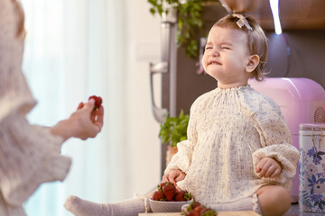 Mom feeding her baby girl with sour strawberries in the kitchen. Rejecting food