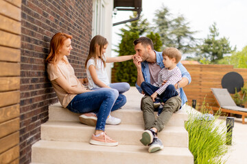 Family with a mother, father, son and daughter sitting outside on the steps of a front porch of a brick house