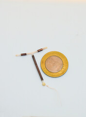 T shape IUD Gold hormone free birth control device beside a coin for size and shape realization on white background. Selective focus.